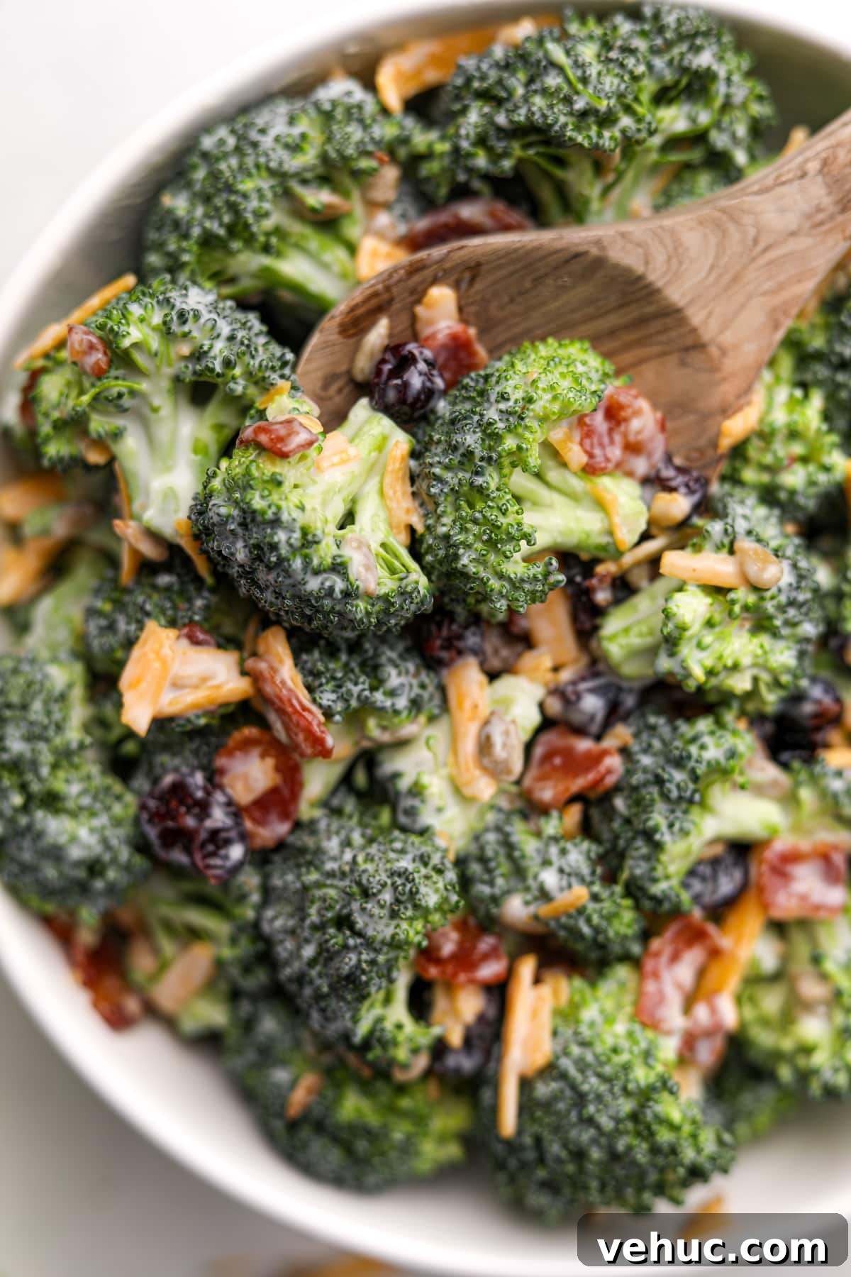 Crispy Broccoli Salad with Creamy Parmesan Dressing 2 A wooden spoon taking a small portion from a large bowl of broccoli salad. It's garnished with bacon and cheddar cheese shreds.
