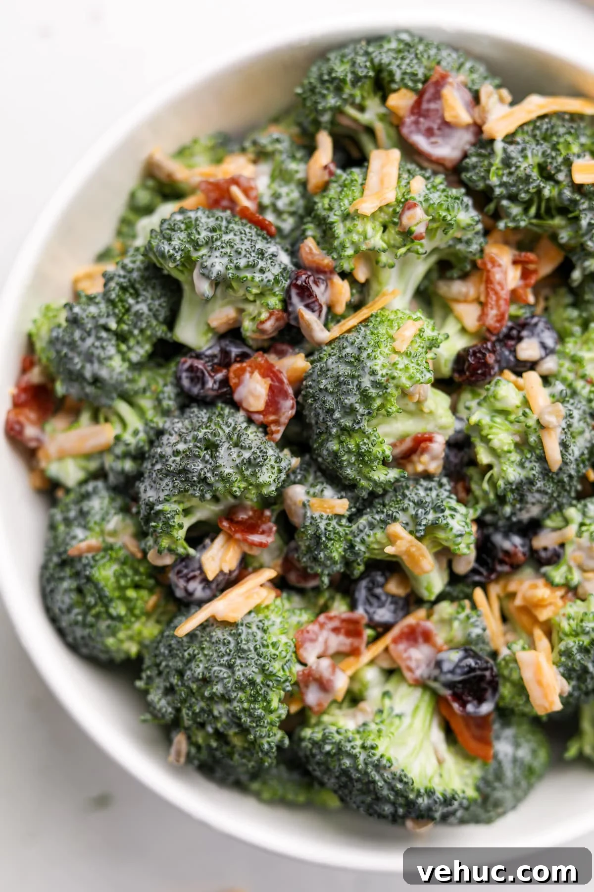 Crispy Broccoli Salad with Creamy Parmesan Dressing 12 A close up of a bowl of broccoli salad featuring bacon crumbles and cheddar cheese shreds.