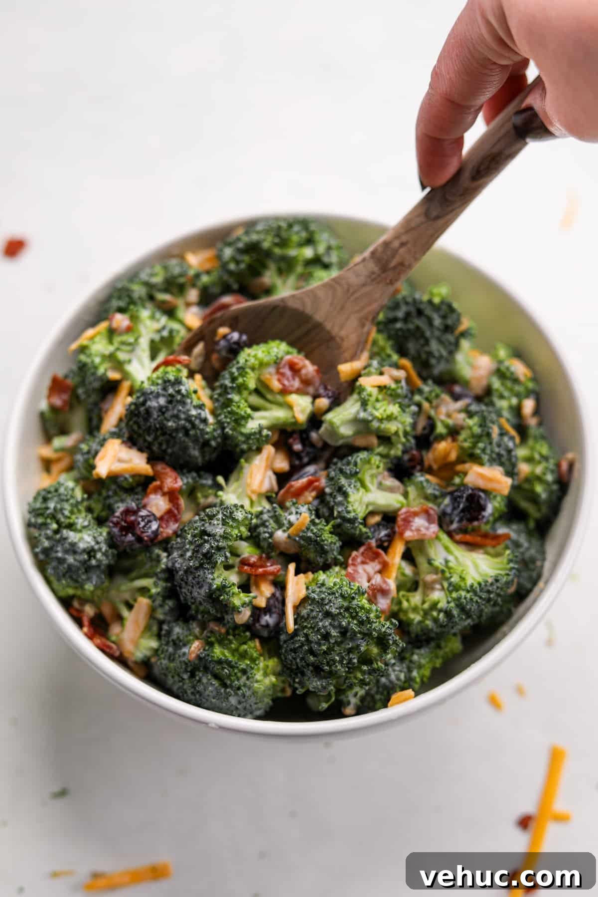 Crispy Broccoli Salad with Creamy Parmesan Dressing 13 A bowl of broccoli salad being stirred with a wooden spoon.