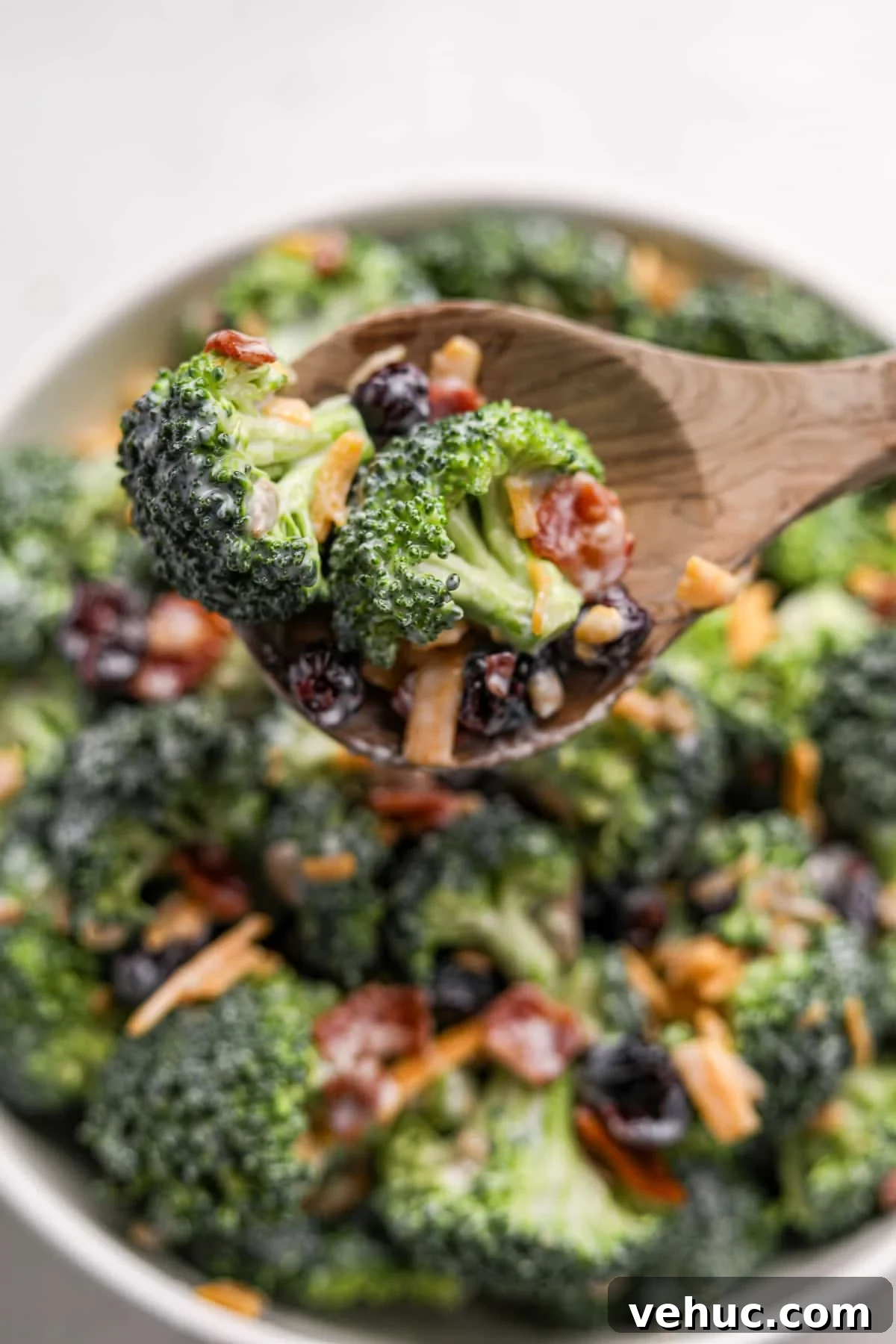 Crispy Broccoli Salad with Creamy Parmesan Dressing 14 Scooping a portion of salad from a large bowl. It features raw broccoli, bacon, and cheese.