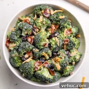 Crispy Broccoli Salad with Creamy Parmesan Dressing 15 A white bowl filled with broccoli salad. It's garnished with cheddar cheese shreds and bacon.