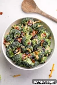Crispy Broccoli Salad with Creamy Parmesan Dressing 21 A white bowl filled with broccoli salad that's been garnished with bacon and cheddar cheese.