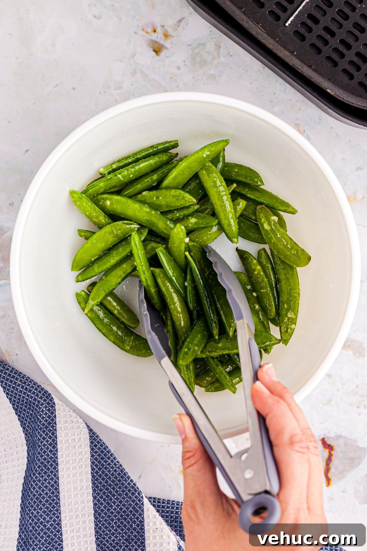 Crispy Air-Fried Sugar Snap Peas in Minutes 5 White bowl with snap peas being tossed in sesame oil and seasonings.