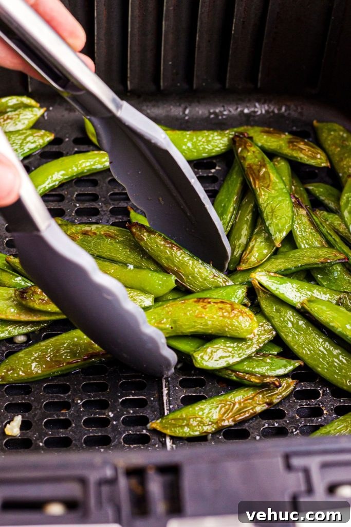 Crispy Air-Fried Sugar Snap Peas in Minutes 8 Air fried snap peas in the air fryer basket after being cooked, being served with tongs