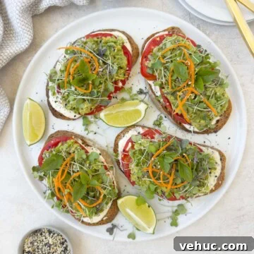Avocado tomato toast with baby greens on top and basil leaves.