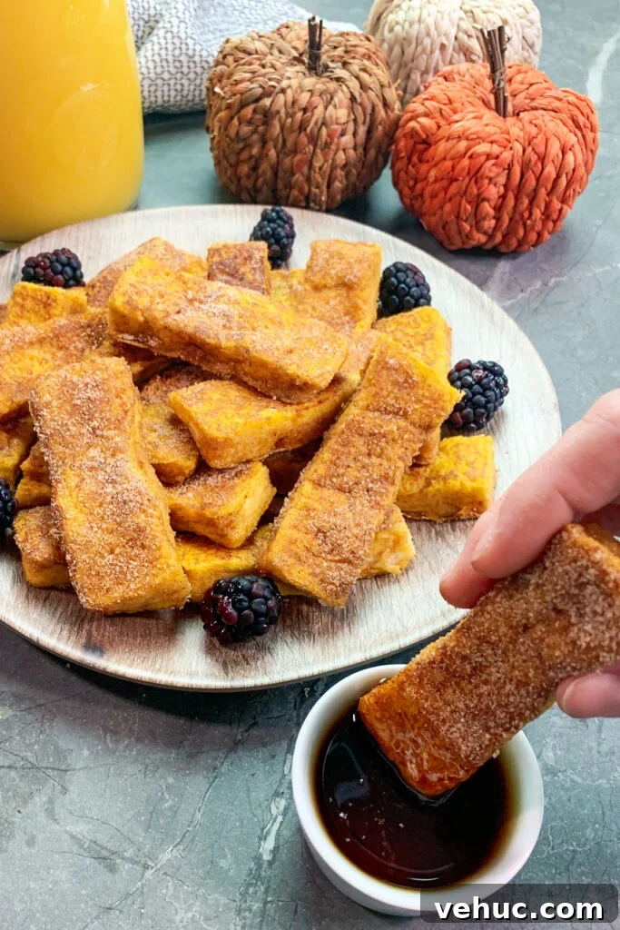 Pumpkin Churro French Toast Sticks Recipe for Fall Brunch 5 Pumpkin bread sticks coated in cinnamon and sugar being dipped into syrup.