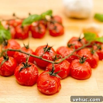 Oven-Roasted Cherry Tomatoes on the Vine: Simple Flavor Boost 3 Roasted cherry tomatoes on the vine with roasted garlic cloves and fresh basil leaves on a wooden butcher block cutting board