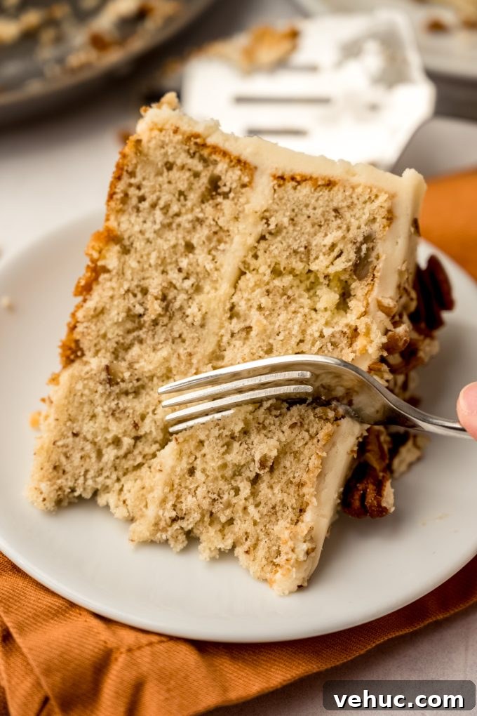 Decadent Butter Pecan Layer Cake Recipe 17 A slice of butter pecan cake on a plate and someone is using a fork to take a bite.