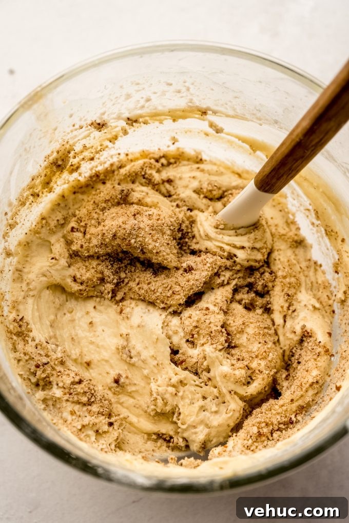 Decadent Butter Pecan Layer Cake Recipe 8 The batter for butter pecan cake in the bowl of a stand mixer with a spatula in it.