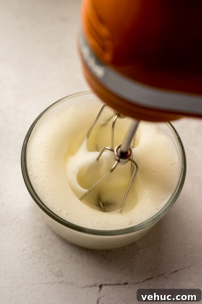 Decadent Butter Pecan Layer Cake Recipe 10 Someone is whipping egg whites in a small glass bowl with a handheld mixer.