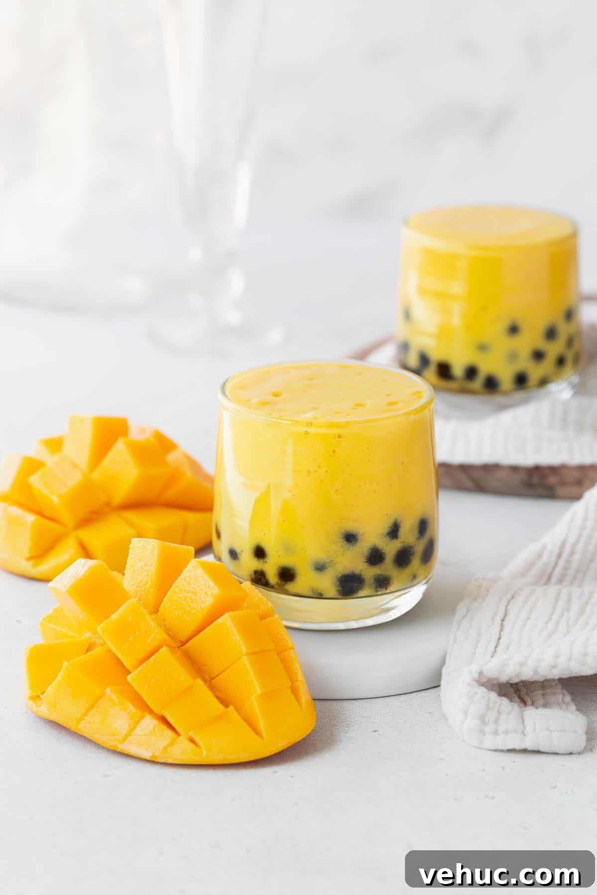 Mango Bubble Tea: Refreshing Homemade Boba Recipe 2 Two glasses of mango boba tea on a white counter next to a cubed up mango.