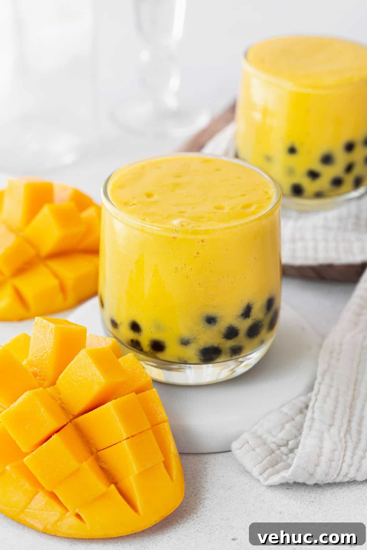 Mango Bubble Tea: Refreshing Homemade Boba Recipe 14 A closeup of a small glass of mango boba tea next to a cubed mango and towel.