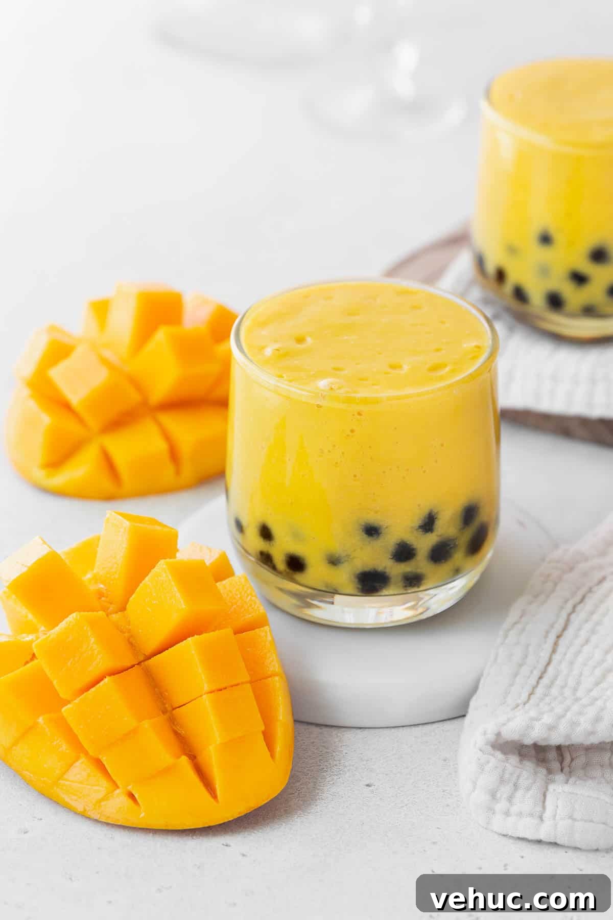 Mango Bubble Tea: Refreshing Homemade Boba Recipe 4 A closeup shot of a small glass of mango boba tea on a white coaster on the counter next to a sliced up mango.