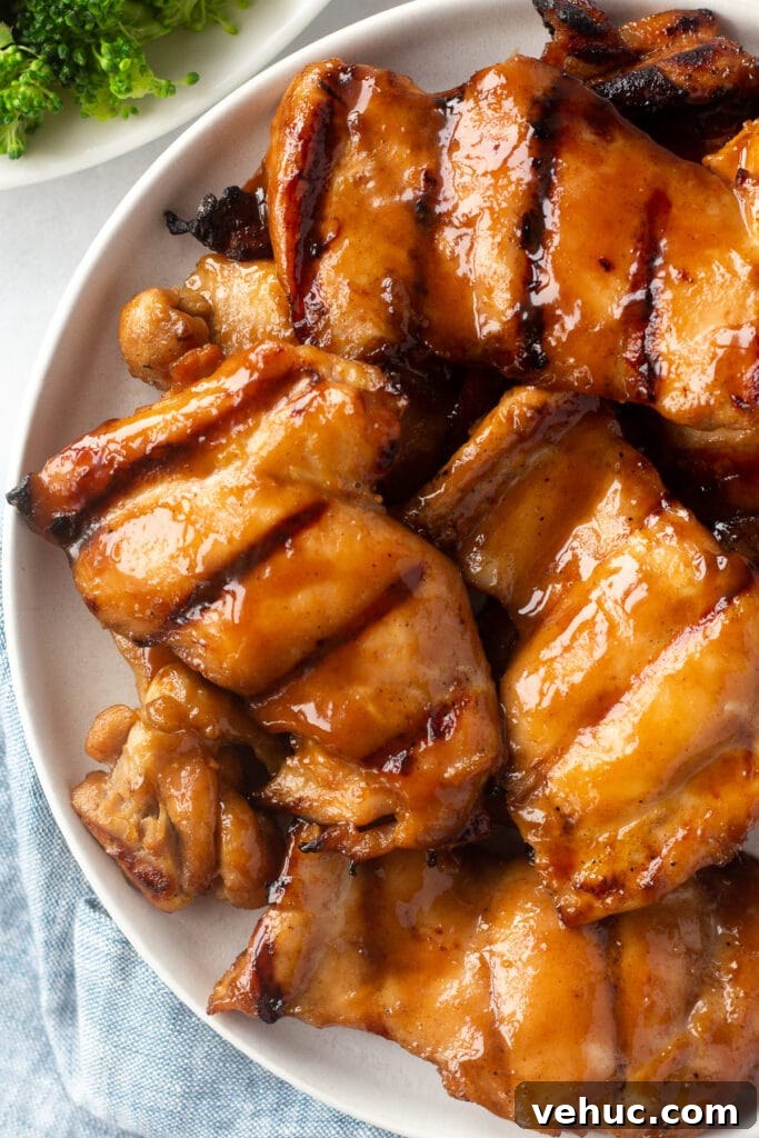 top down shot of gluten free grilled chicken thighs on a white plate. A plate of broccoli is in the upper left corner and a blue cloth napkin is in the bottom left corner.