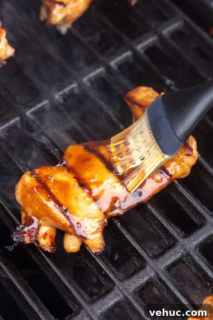 A boneless skinless chicken thigh on the grill being brushed with sauce.