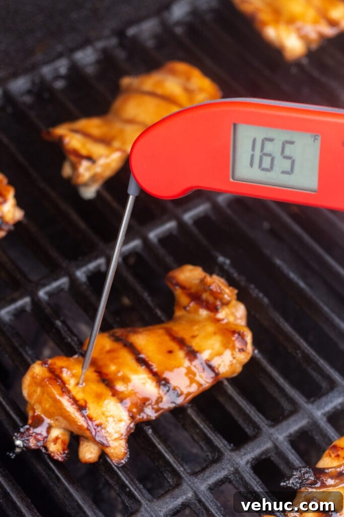 An instant read thermometer measuring the internal temp of chicken thighs on the grill.