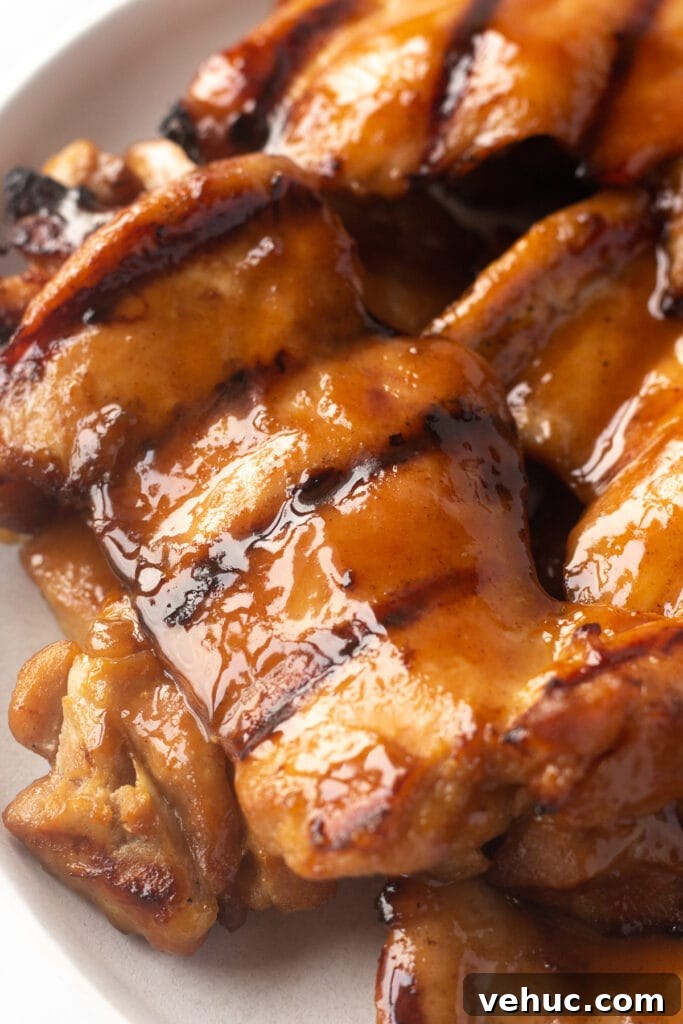 Close up of grilled boneless skinless chicken thighs on a white plate.
