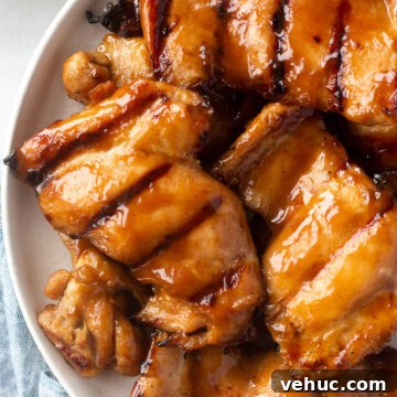top down shot of gluten free grilled chicken thighs on a white plate. A plate of broccoli is in the upper left corner and a blue cloth napkin is in the bottom left corner.