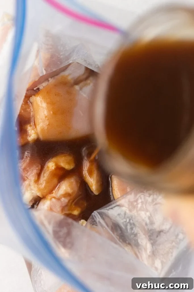 pouring brown marinade from a mason jar into a ziploc bag with raw boneless skinless chicken thighs in it.