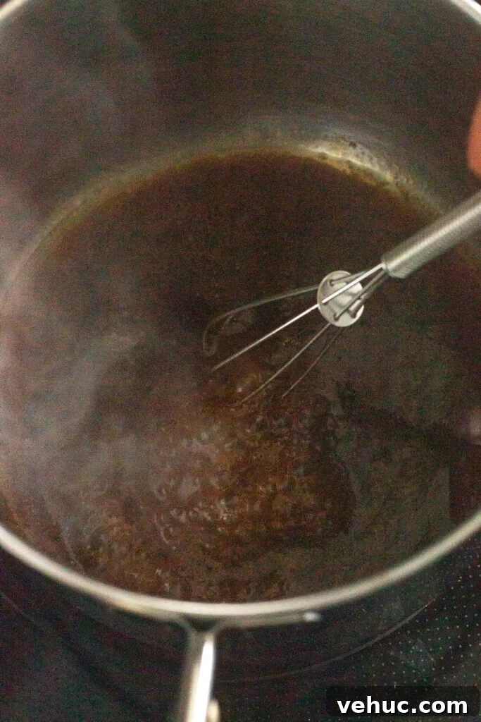 A close up of a brown chicken marinade being boiled in a small sauce pan with a whisk.