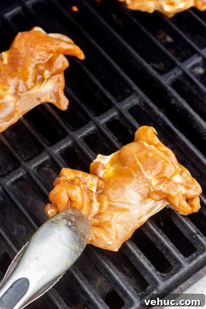 A pair of tongs placing raw chicken thighs on a hot grill.