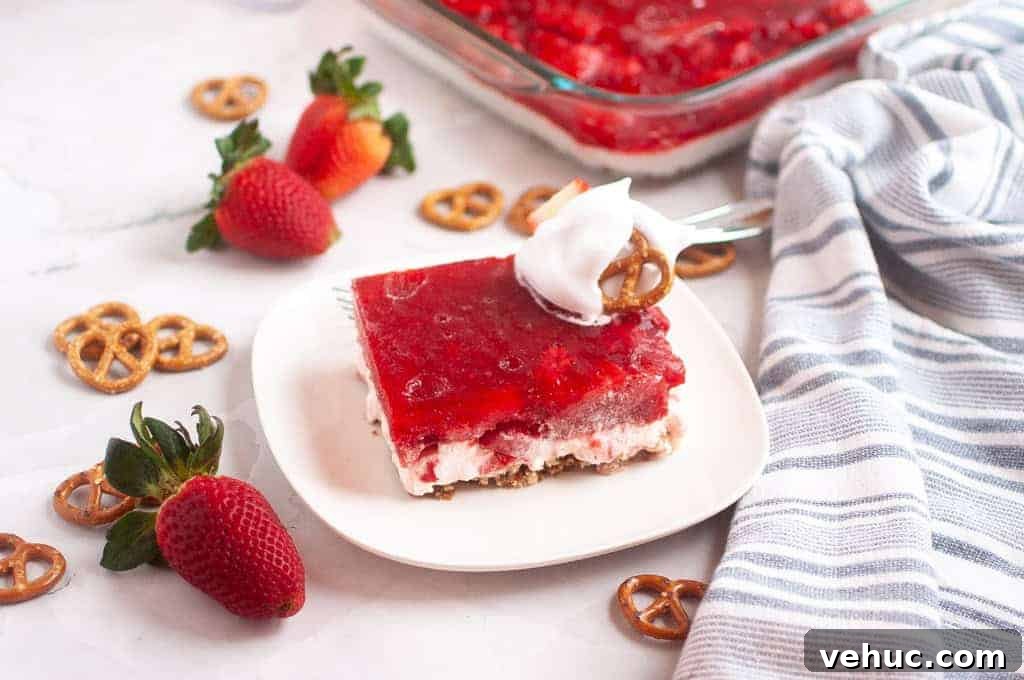 11 Strawberry Recipes That Highlight Their Sweet-Tart Flavor 3 A slice of Strawberry Pretzel Salad topped with whipped cream and a pretzel sits on a white plate.