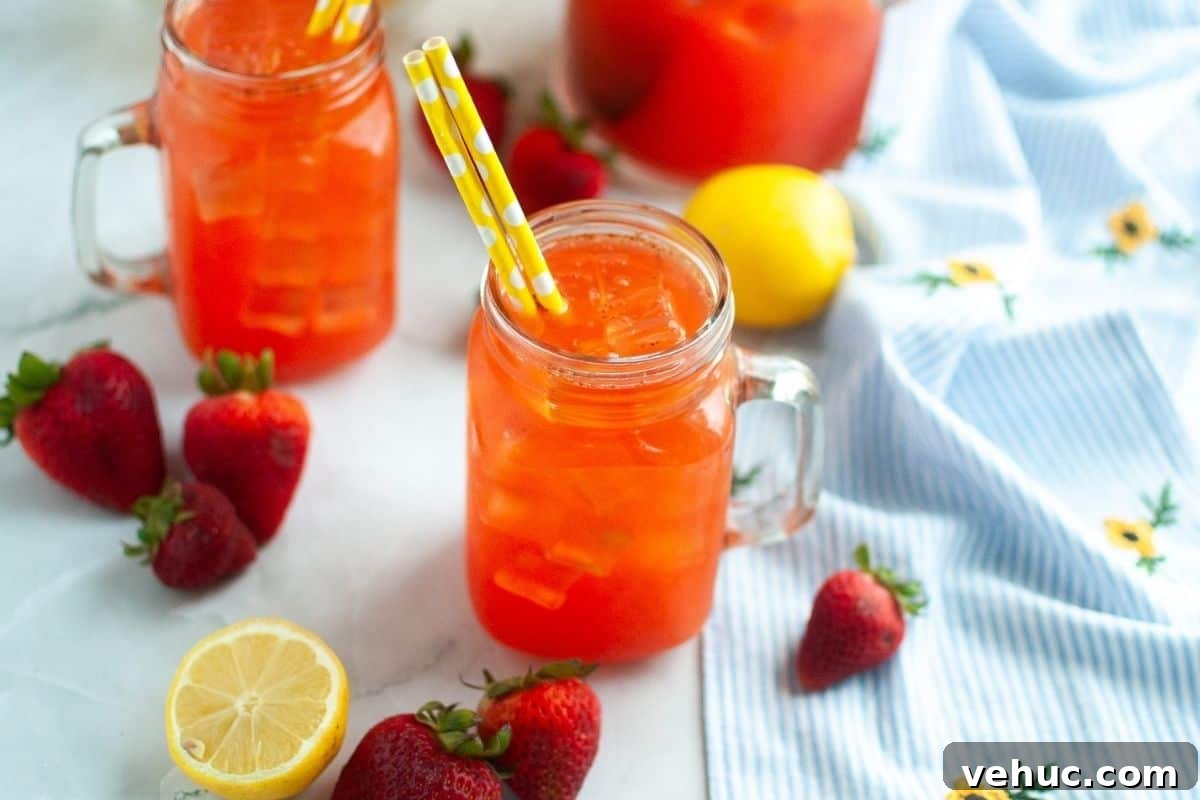 11 Strawberry Recipes That Highlight Their Sweet-Tart Flavor 5 Glass mason jars filled with iced strawberry lemonade on a table, surrounded by fresh strawberries, a halved lemon, and a blue floral cloth.