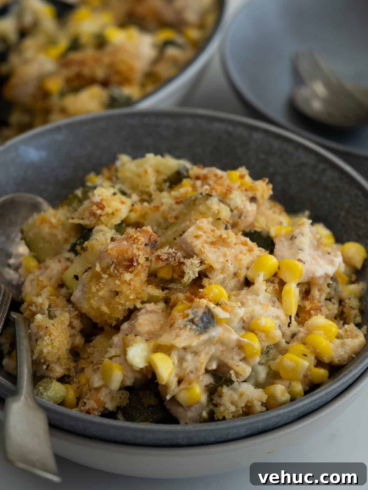 Creamy Chicken and Zucchini Casserole for Weeknight Dinner 6 Chicken pieces, zucchini, corn in a creamy cheesy sauce and crunchy bread topping served in a bowl.