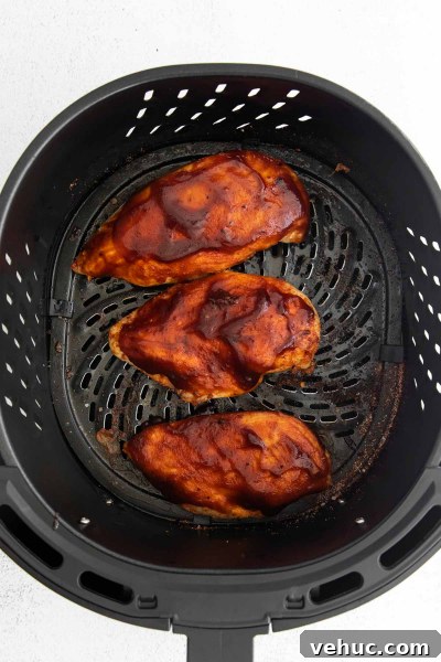Crispy Air Fryer BBQ Chicken Recipe for Tender, Smoky Flavor 6 chicken breast in air fryer basket with bbq sauce rubbed over it