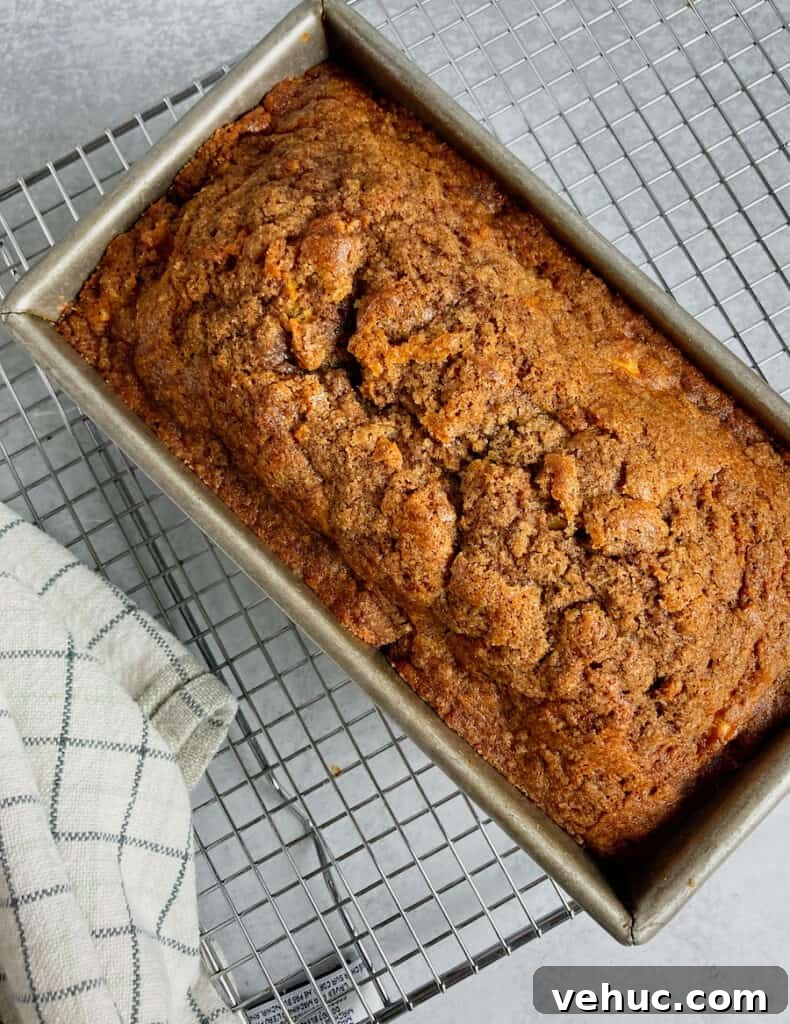 Dutch Apple Bread with Streusel Topping — Soft, Cinnamon-Loaf Recipe 2 A loaf of apple bread in a pan on a cooling rack.