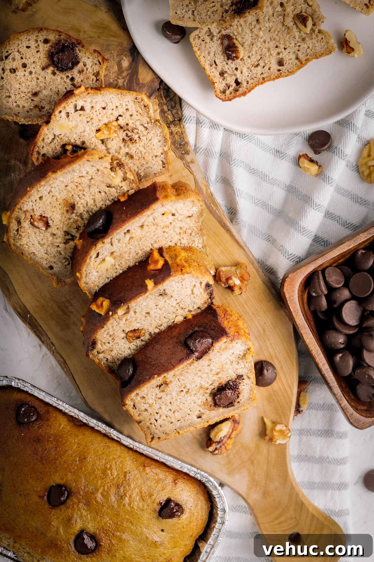 Closeup overhead photo of air fryer banana bread sliced on a wood board with striped towel in the background