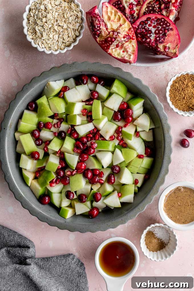 Apple Cranberry Crisp: Gluten-Free Vegan Recipe for Fall Dessert 4 Chopped granny smith apples, cranberries and pomegranate arils mixed together in a grey pie plate.