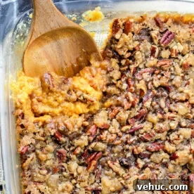 Creamy Sweet Potato Casserole Using Canned Yams 7 A glass dish with a delectable sweet potato casserole recipe featuring canned yams, topped with crunchy pecans and accompanied by a wooden spoon.
