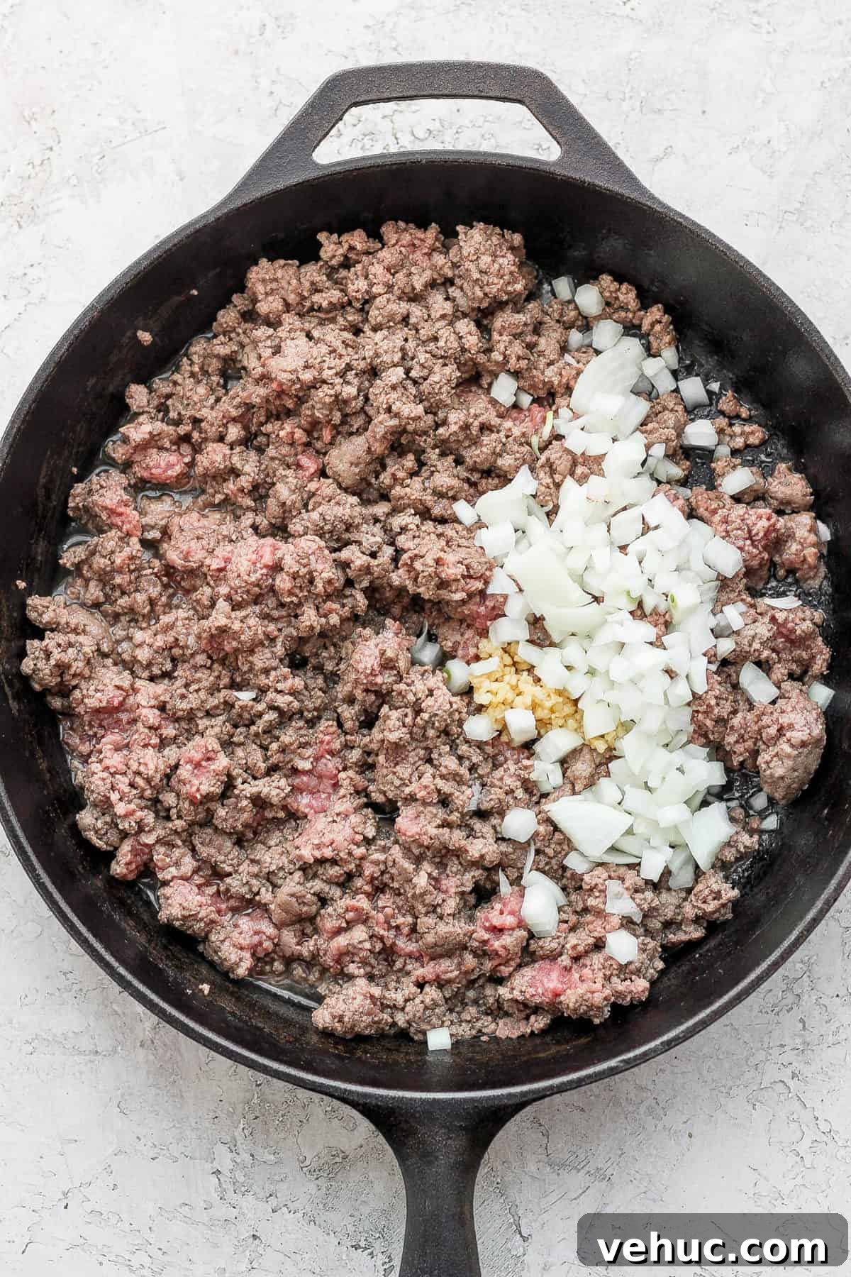 Ground beef in a skillet with diced onion and minced garlic.
