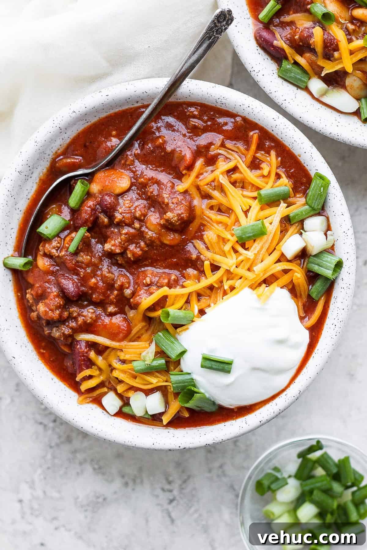 Slow cooker chili in a bowl topped with sour cream, shredded cheese and diced green onion.