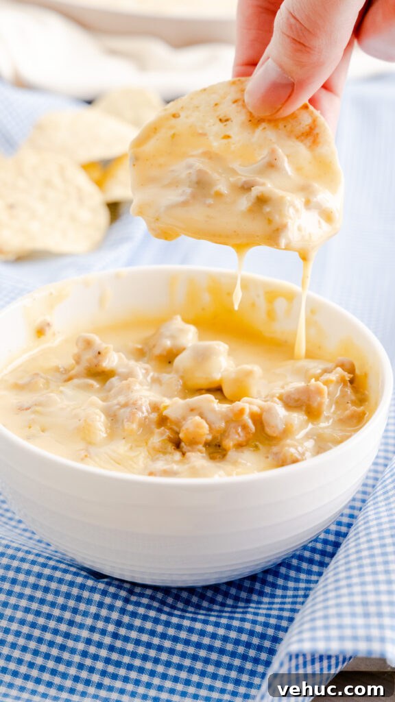 Tortilla chip scooped with sausage queso dip with cheese dripping into bowl. 