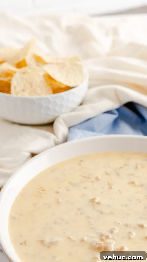 White serving bowl of instant pot cheese dip made with sausage on blue checkered napkin. 