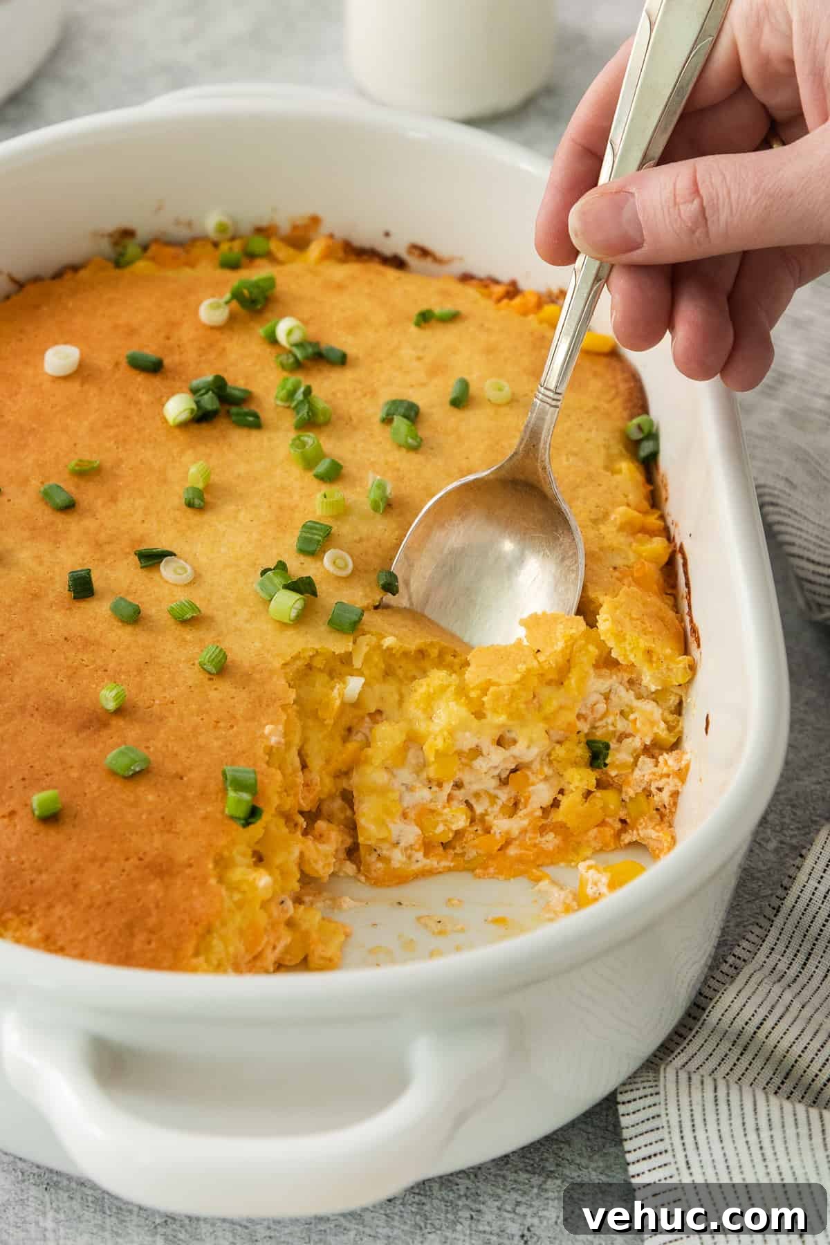 Creamy Cheddar Corn Casserole Recipe for Comforting Sides 3 a person holding a spoon in a casserole dish.