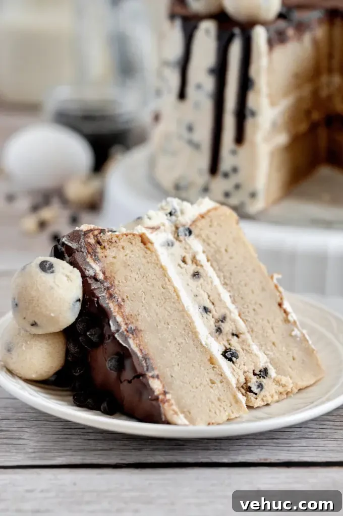 A cookie dough cake covered in cream cheese cookie dough frosting with dark brown chocolate ganache drip and topped with edible cookie dough balls.