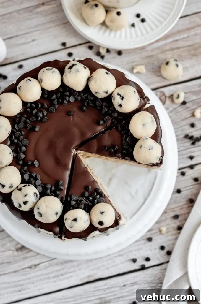 A cookie dough cake covered in cream cheese cookie dough frosting with dark brown chocolate ganache drip and topped with edible cookie dough balls.