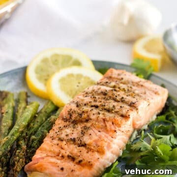 Grilled salmon on a bed of herbs with slices of lemon in the background.