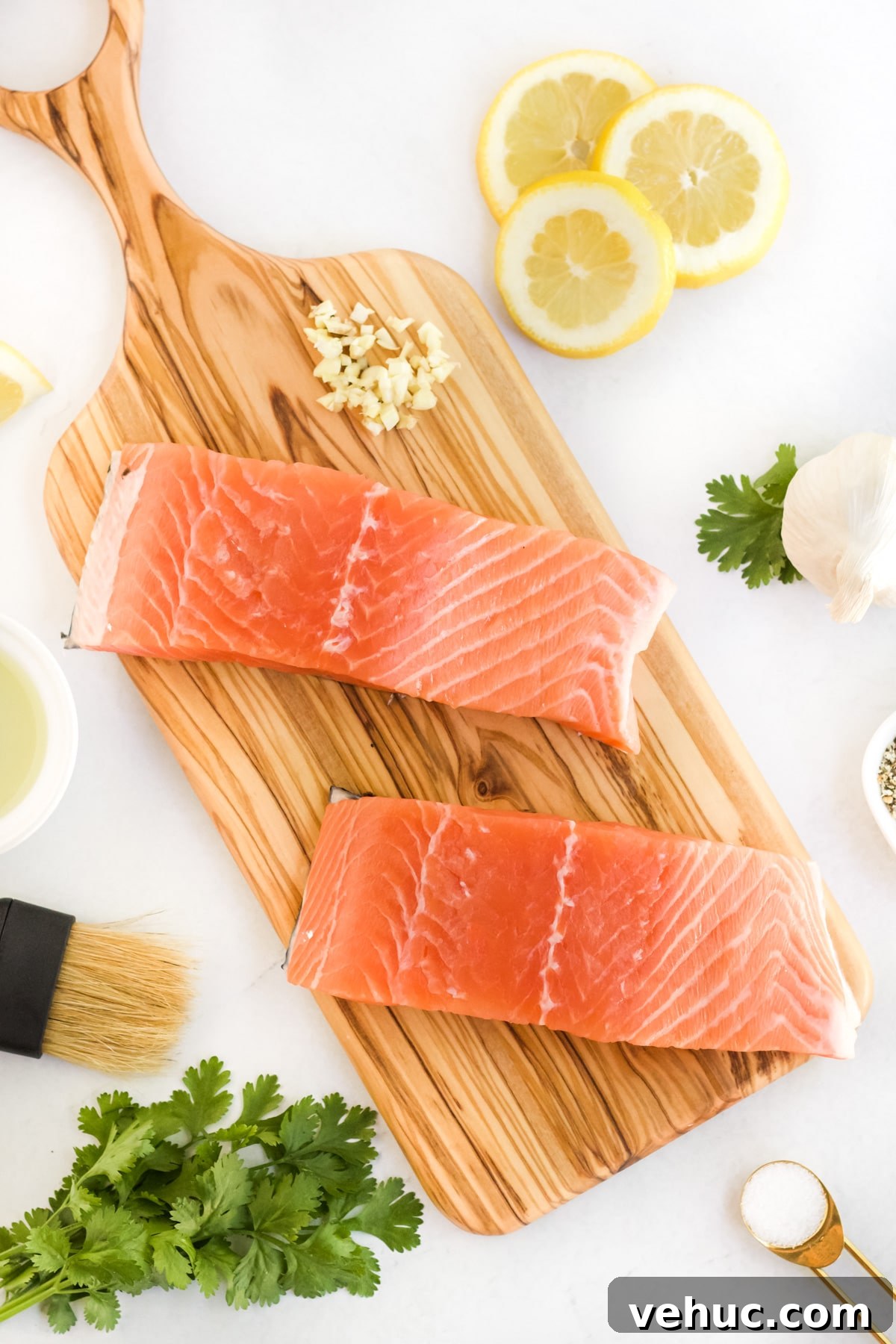 Raw salmon being prepared for the grill on a cutting board will all the ingredients around it. 