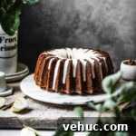Brown bundt cake with white glaze on a marble platter with apple branches in foreground