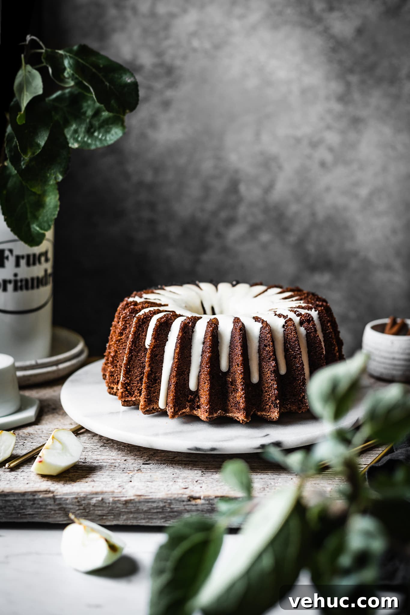 Moist Applesauce Bundt Cake Recipe for Fall Baking 5 Brown bundt cake with white glaze on a marble platter with apple branches in foreground