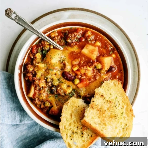 A bowl of shepherd's pie chili topped with herbs, served with a spoon and two slices of toasted bread on the side.