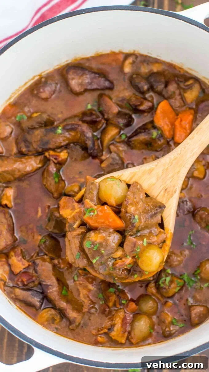 Classic Beef Bourguignon Recipe: Tender Braised Beef in Red Wine 5 Homemade Beef Bourguignon in a Dutch oven with a serving wooden spoon filled with tender meat and veggies