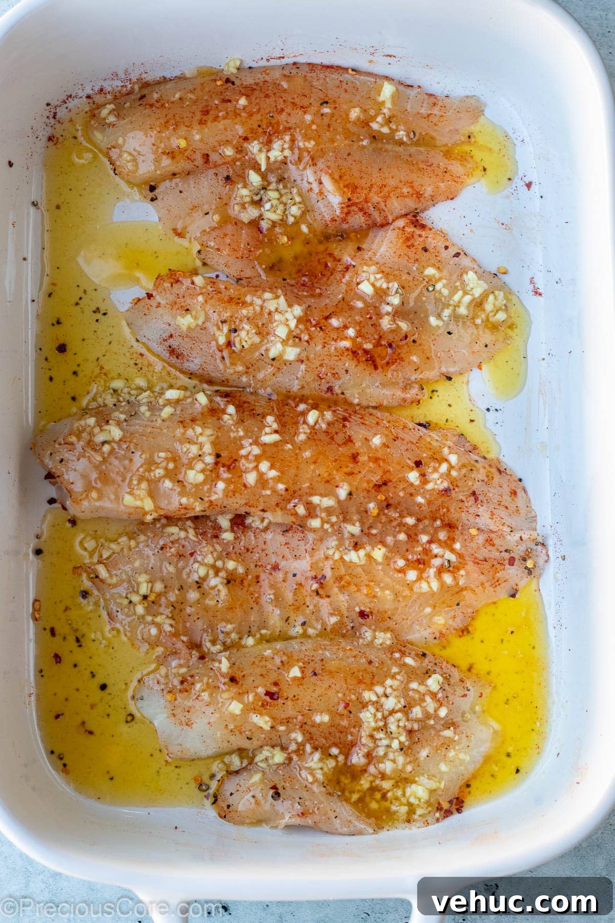Garlic Butter Tilapia Recipe with Lemon and Herbs 7 Raw fish fillets covered with garlic butter sauce.
