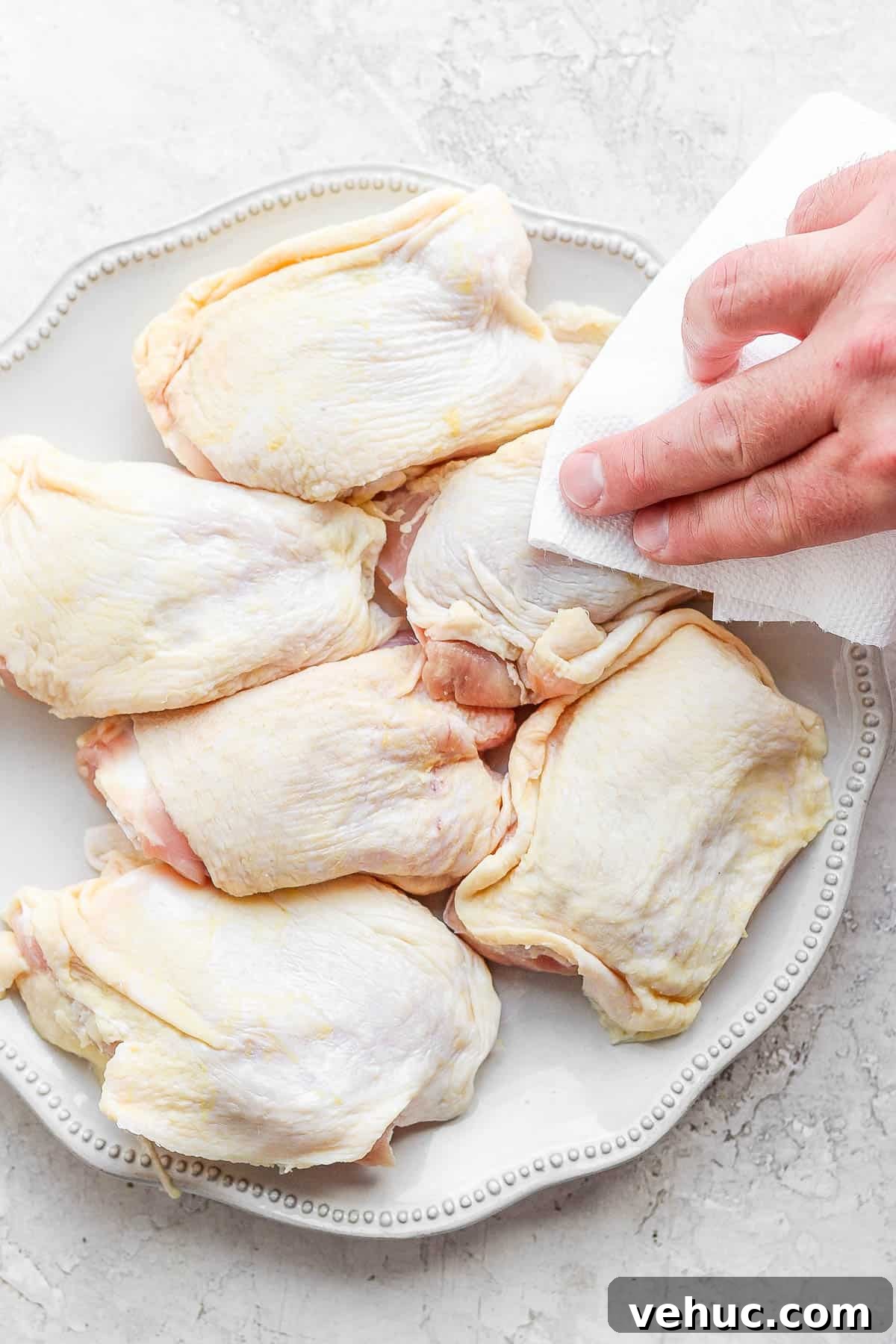A plate of chicken thighs with someone patting them dry with a clean paper towel.