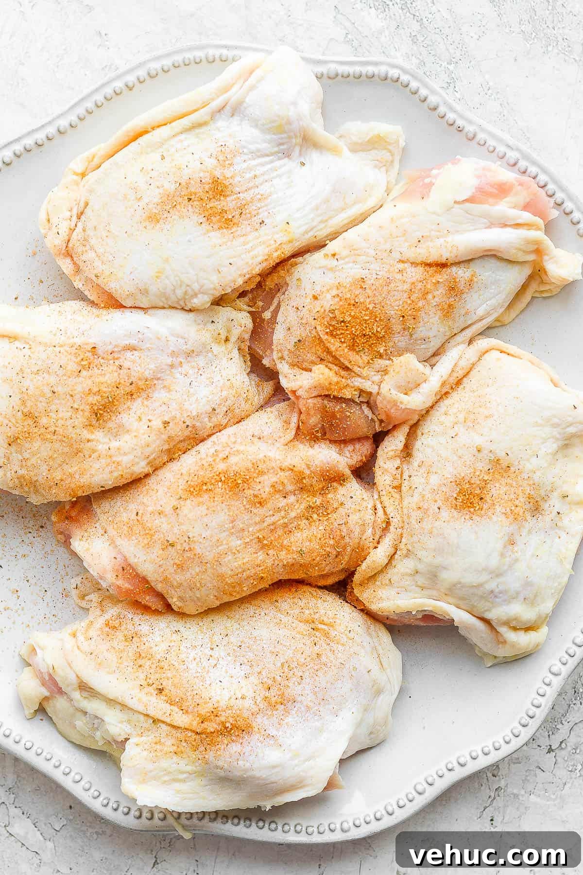 A plate of raw chicken thighs covered in a smoked chicken dry rub. 