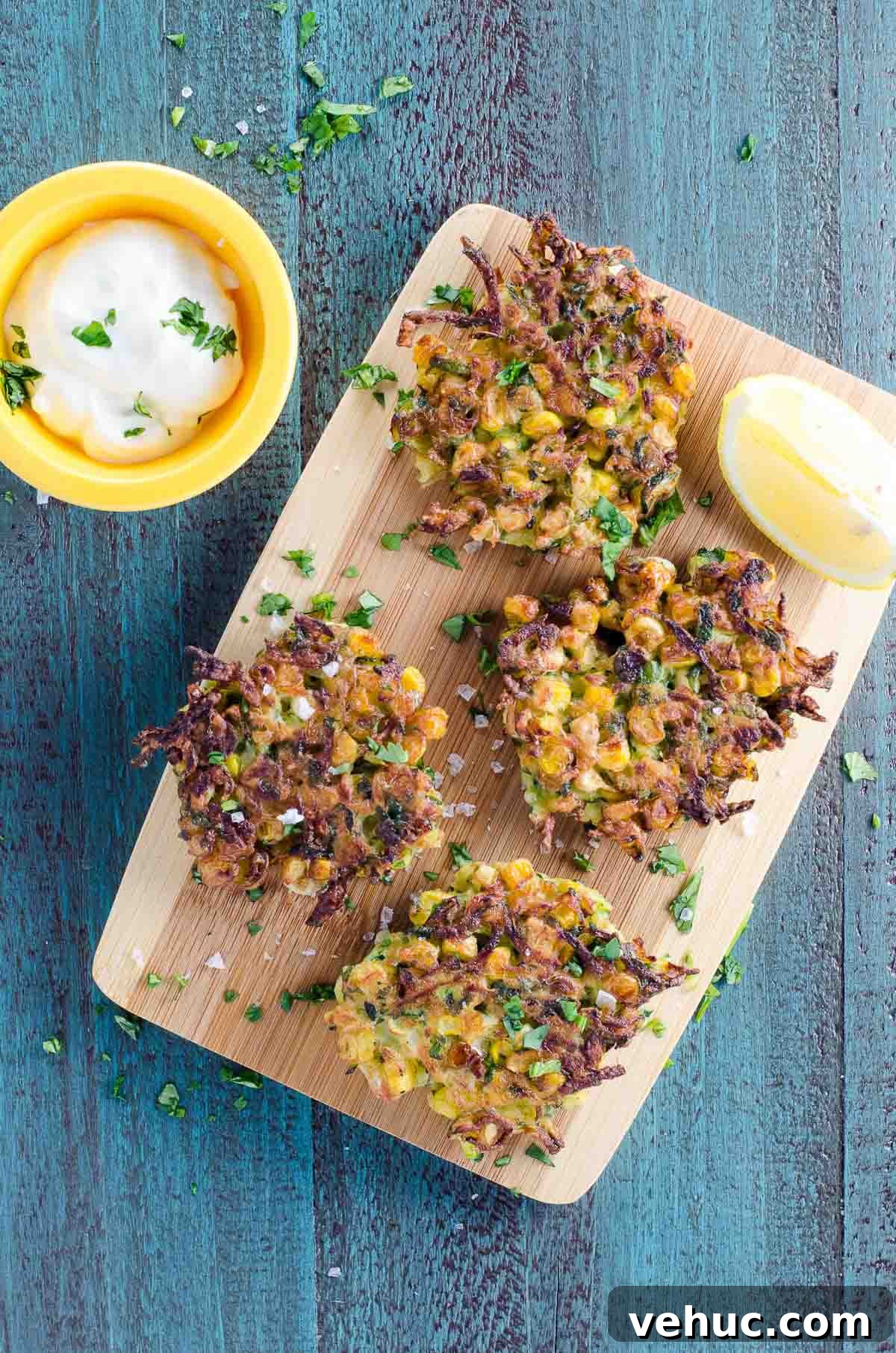 Crispy Zucchini and Sweet Corn Fritters Recipe 2 zucchini and corn fritters with a lemon wedge and sour cream